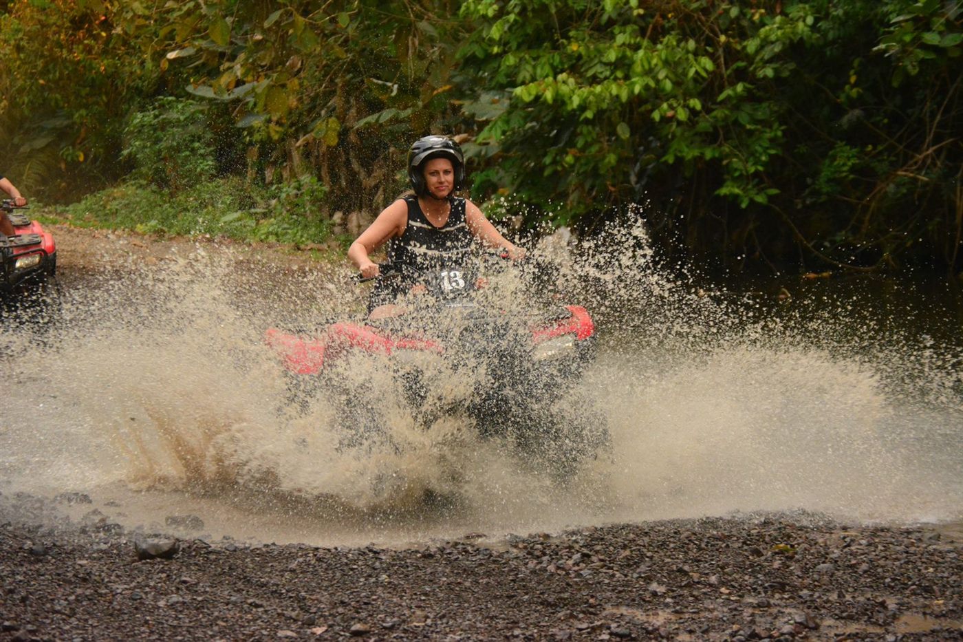 Woman driving an ATV through a large water splash